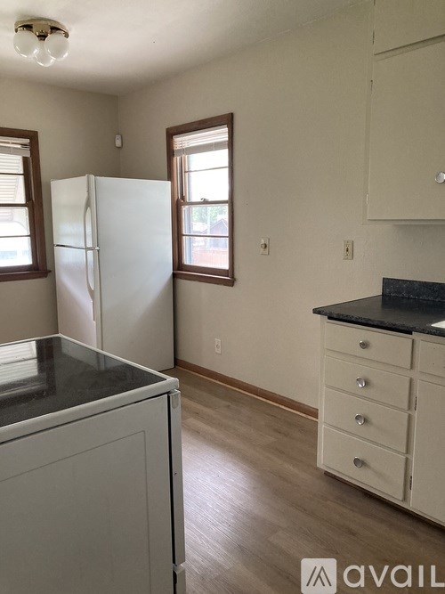 A kitchen with a white fridge, white cabinets, and a black countertop.