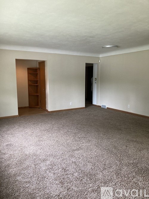A carpeted room with a door and a shelf.