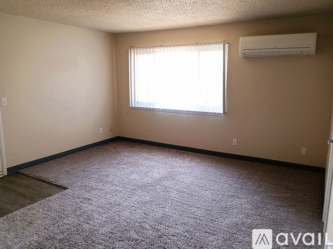 A room with a carpeted floor, a window with blinds, and an air conditioner mounted on the wall.