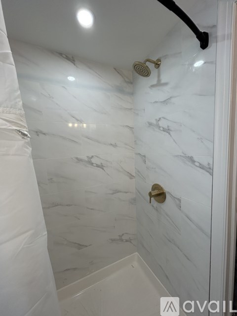 A white marble bathroom with a gold shower head.