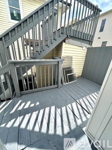 A deck with a metal railing and wooden steps leading to a house.