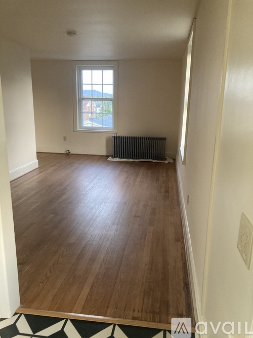 A room with wooden floors and a window with a view of the street outside.
