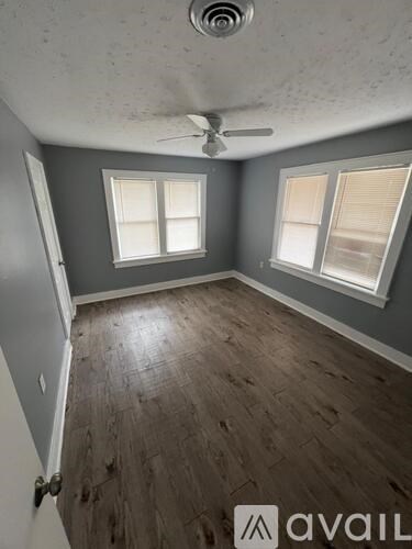 A room with a ceiling fan and two windows.