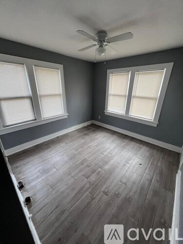 A room with a ceiling fan and two windows.