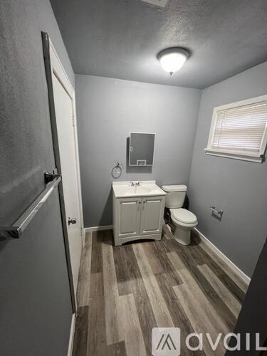 A small bathroom with a toilet, sink, and wood flooring.