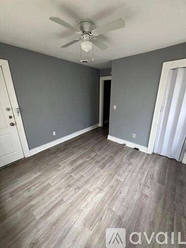 A room with a ceiling fan and light fixture, grey walls, and a wooden floor.