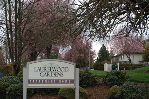 A sign for Laurelwood Gardens Apartment Homes is in front of a flowering tree.