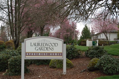 A sign for Laurelwood Gardens Apartment Homes stands in front of a flowering tree.