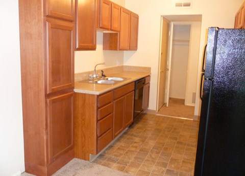 A kitchen with wooden cabinets and a black refrigerator.