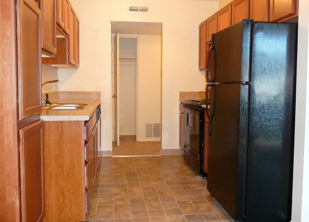 A kitchen with a black refrigerator and wooden cabinets.
