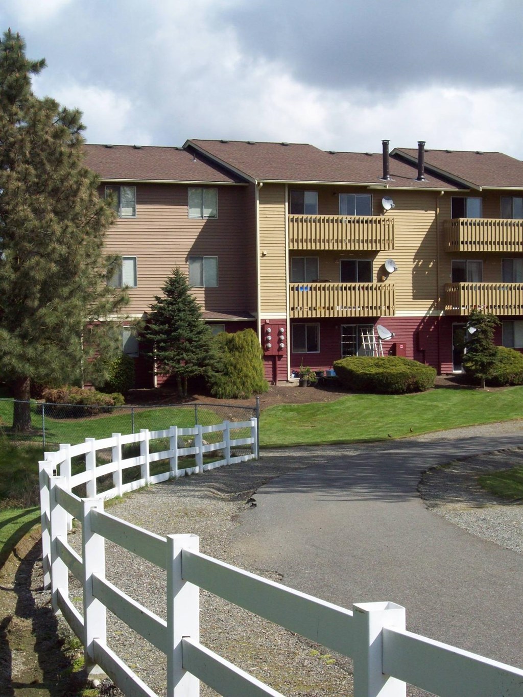 A white picket fence in front of a brown and yellow apartment building.