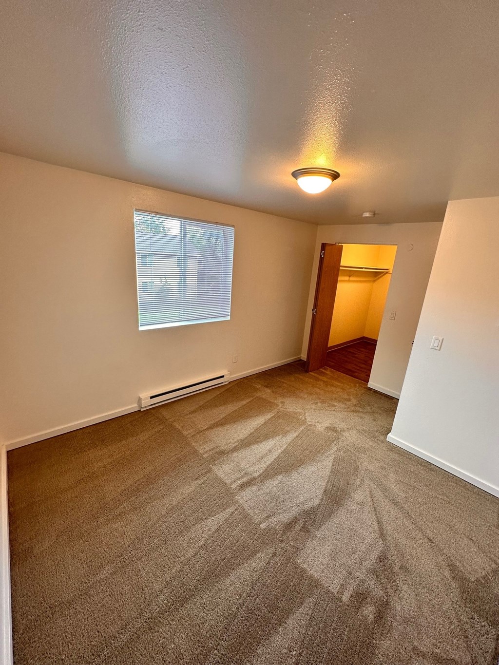 A room with a carpeted floor and a window with blinds.