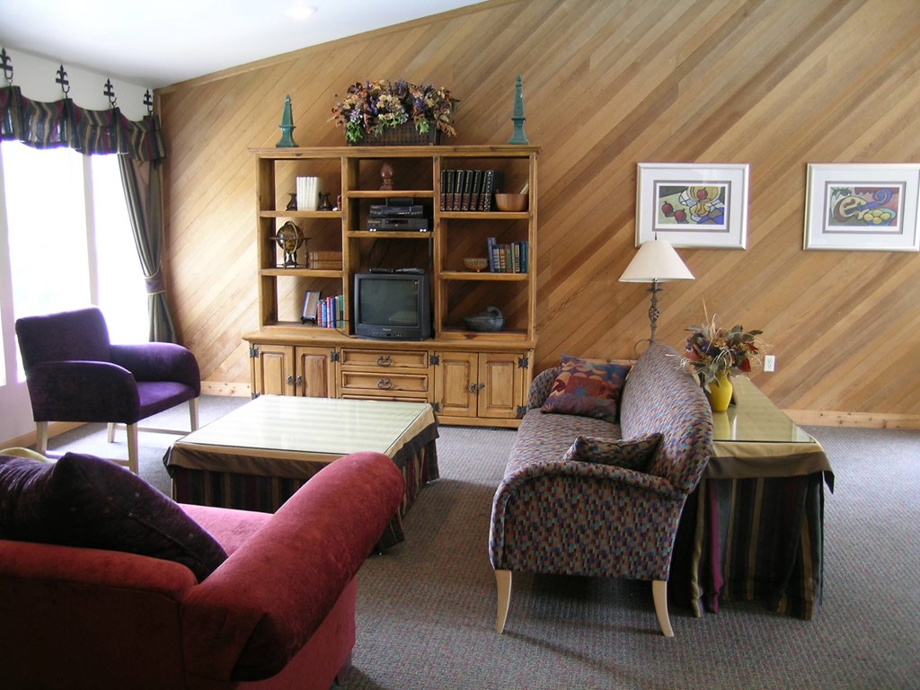 A living room with a red couch, a coffee table, a chair, a bookshelf, and a lamp.