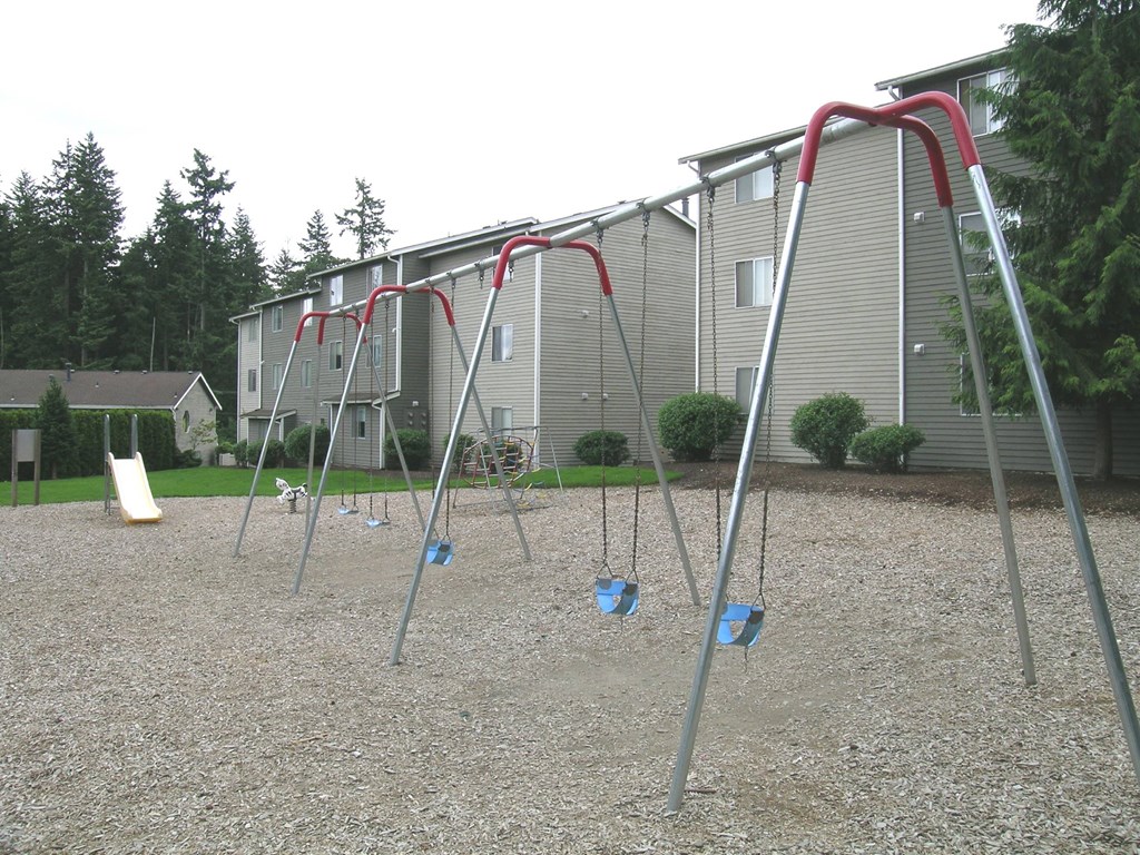 A playground with swings and a slide in front of apartment buildings.