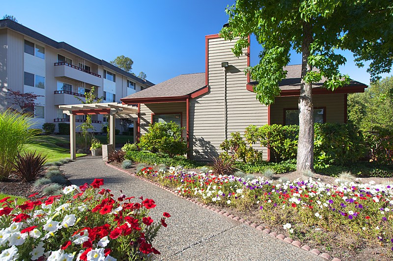A building with a red roof is surrounded by flowers and trees.