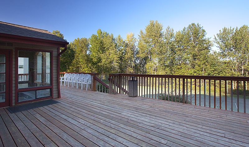A wooden deck with a red building and trees in the background.