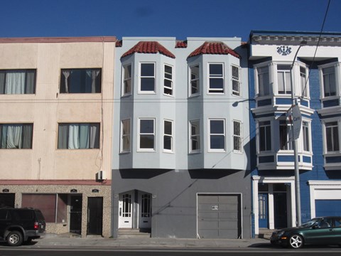 A row of three-story buildings with a car parked in front of them.