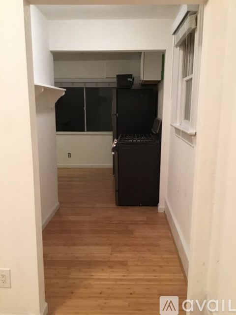 A black refrigerator in a kitchen with white walls and wooden floors.