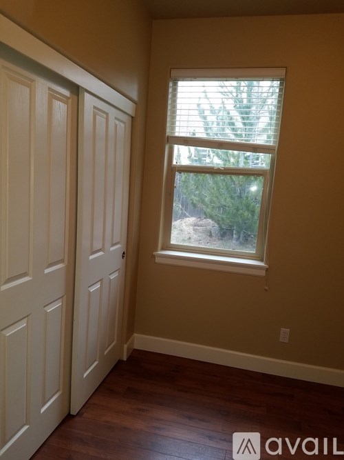 A room with a brown floor and a window with blinds.