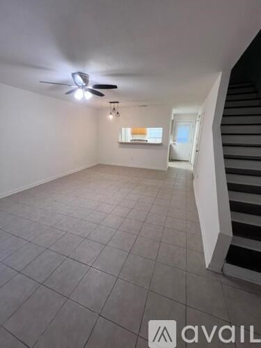 A room with a staircase on the right side and a ceiling fan on the left.