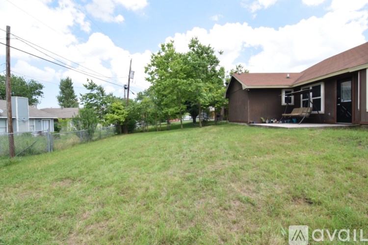 A backyard with a fence, a tree, and a house.