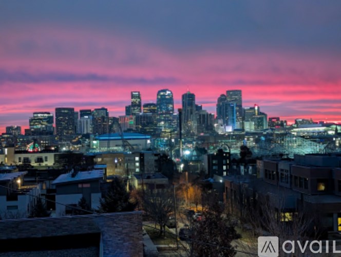 A city skyline at dusk with buildings illuminated against a pink and purple sky.