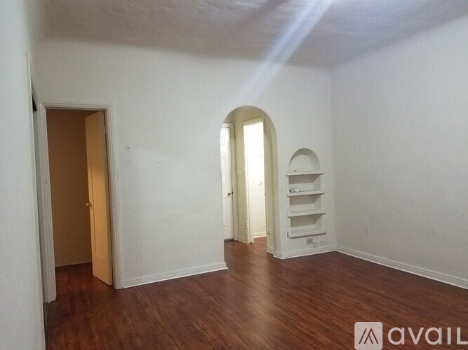 A room with a wooden floor and white walls, with a door on the left and a window with a white frame on the right.