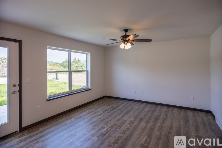A room with a ceiling fan and a large window overlooking a green area.