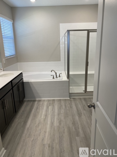 A bathroom with a bathtub, sink, and wooden flooring.