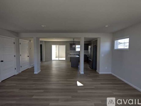 A spacious room with wooden floors and white walls, with a kitchen area visible in the distance.