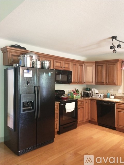 A black refrigerator stands in a kitchen with wooden cabinets.