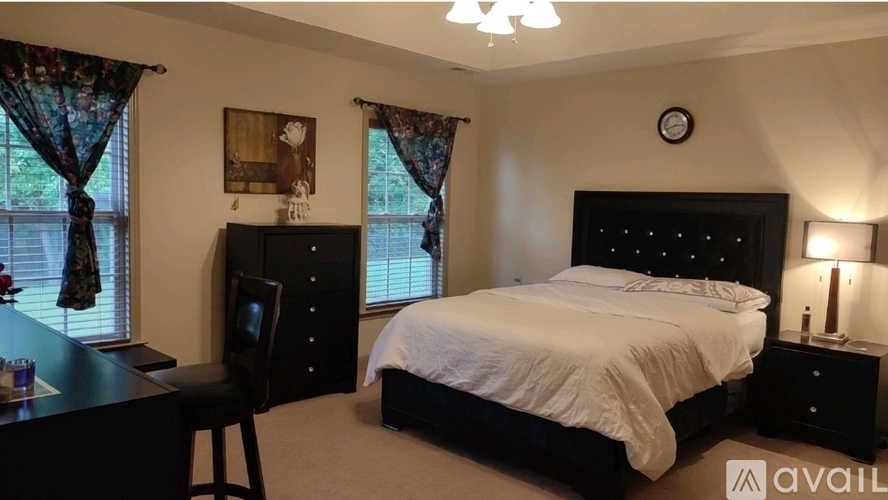 A bedroom with a large bed, a desk, and a window with curtains.