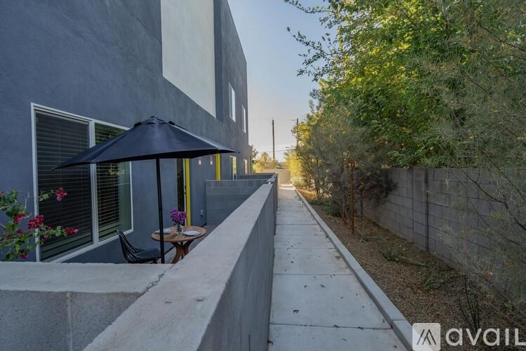 A patio with a table and chairs is on the left side of a concrete walkway.