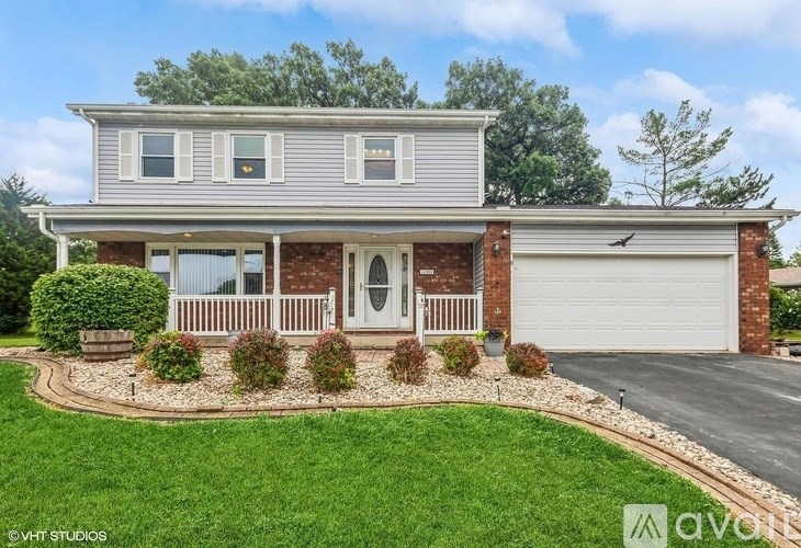 A house with a grey roof and a white door is surrounded by a green lawn.