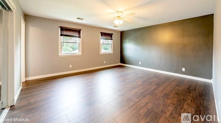 A room with wooden flooring and two windows.