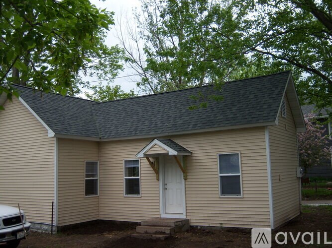 A small house with a white door and windows is surrounded by trees.