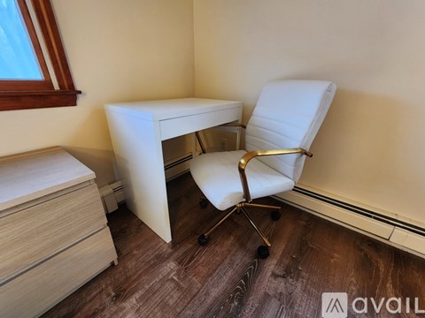 A white chair with wheels is placed next to a white desk with drawers.