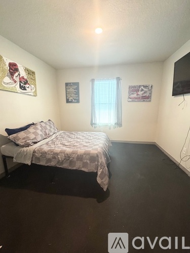 A bedroom with a bed, a window with curtains, and a flat-screen TV mounted on the wall.