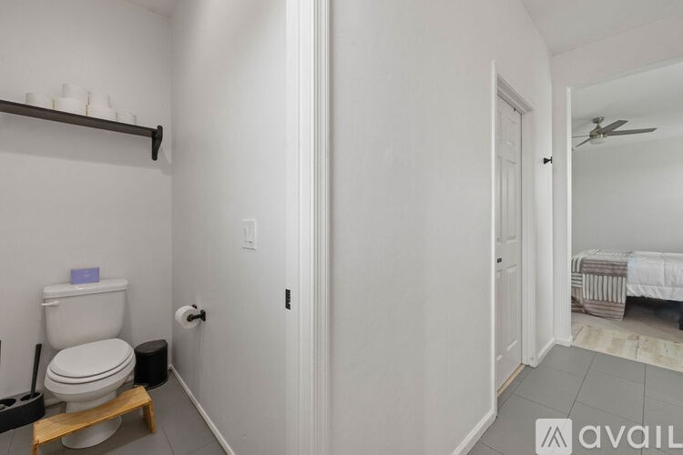 A bathroom with a toilet, a towel rack, and a bed in the other room.