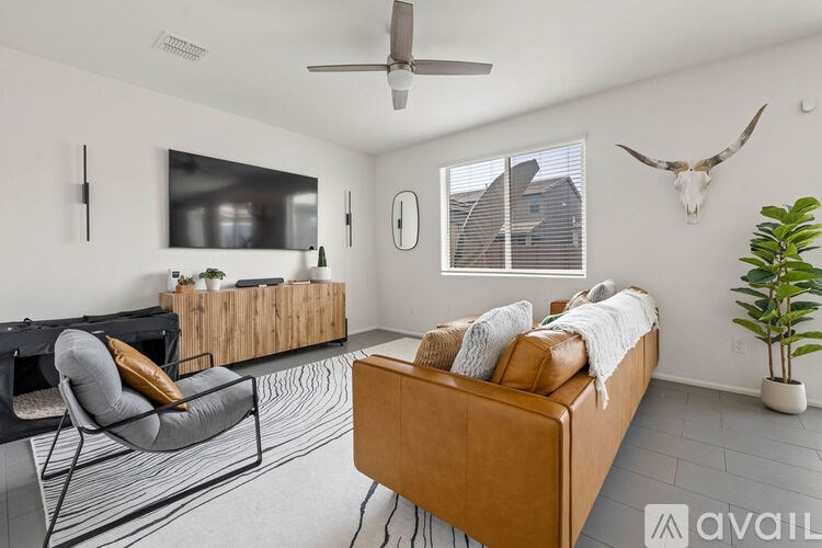 A living room with a brown leather couch, a grey chair, a wooden coffee table, a ceiling fan, and a wall decoration of a deer skull.