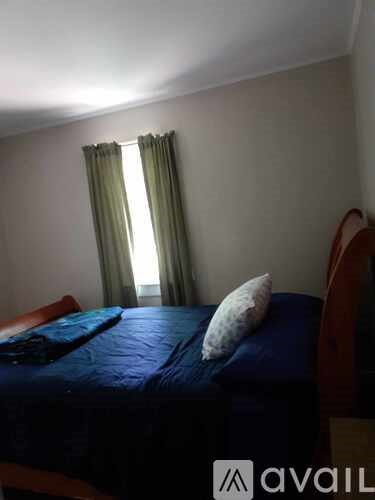 A bedroom with a bed, pillow, and window with curtains.