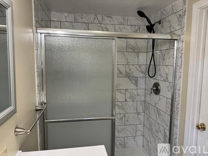 A shower with a glass door and a marble tile wall.