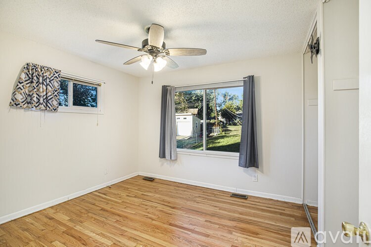 A room with a ceiling fan and a window with a view of a backyard.