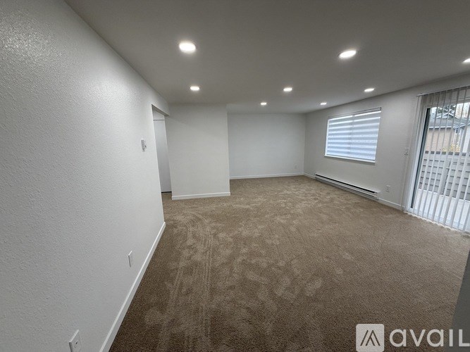 A room with a grey carpet and a window with a view of a fence and trees.
