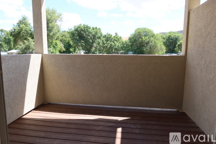 A balcony with wooden flooring and a view of trees and sky.