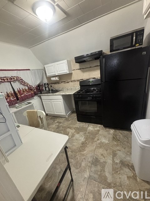 A kitchen with a black fridge, white cabinets, and a white counter.