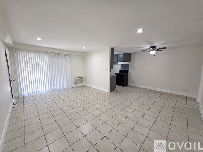 A spacious room with a fan and a kitchenette in the background.