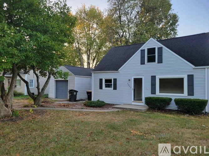 A house with a blue siding and a black roof is surrounded by trees and bushes.