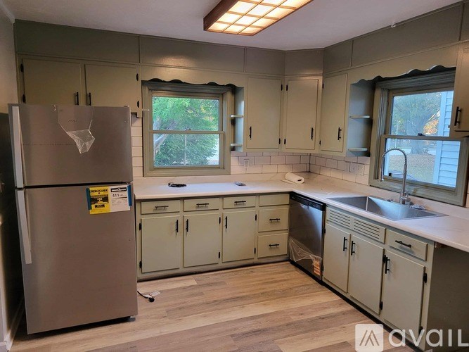 A kitchen with a refrigerator, cabinets, and a window.
