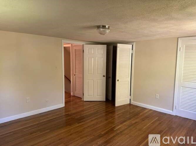 A room with wooden floors and white walls, with a door in the middle and another one to the right.